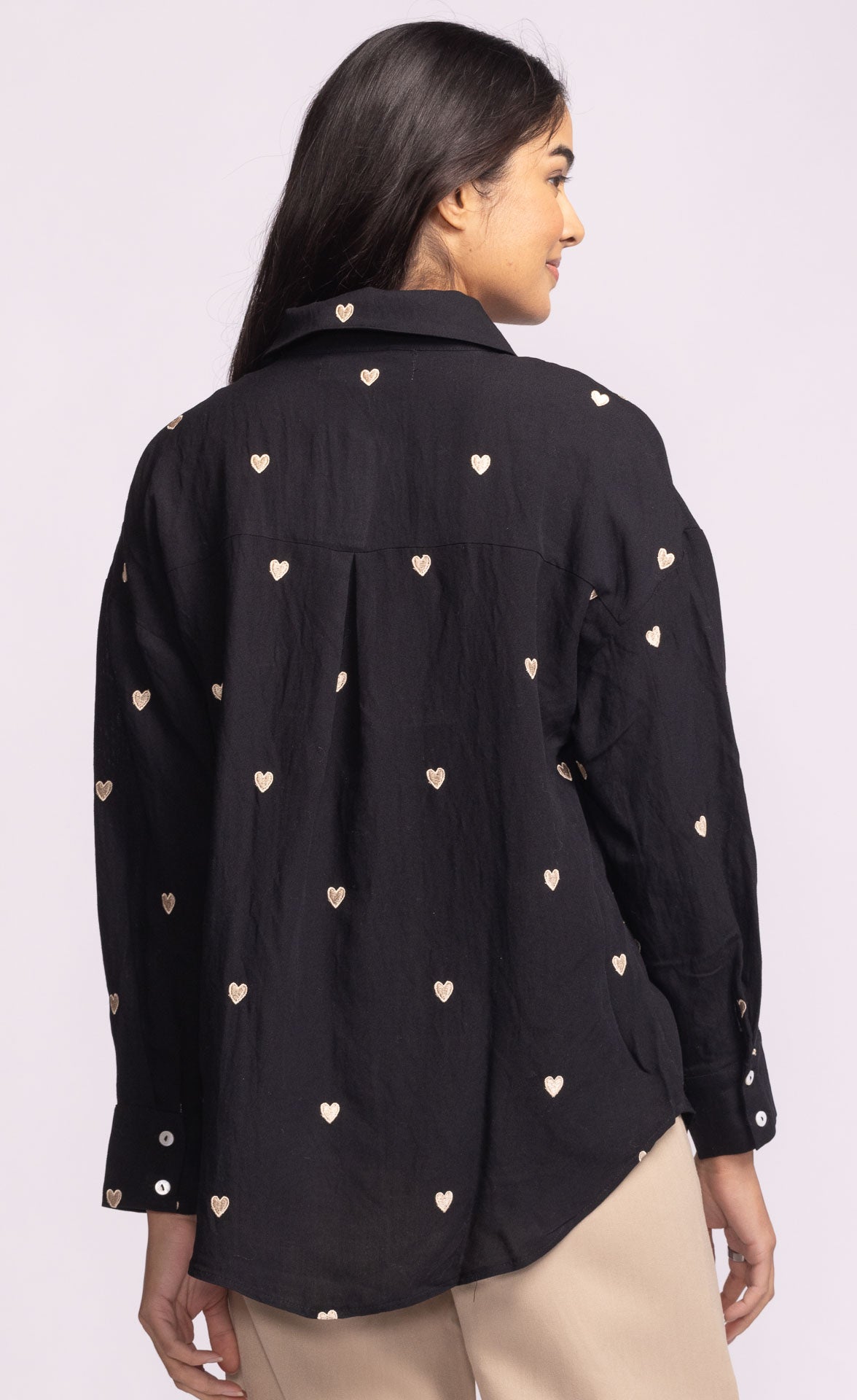 Black shirt with heart patterns worn by a person on a light purple background