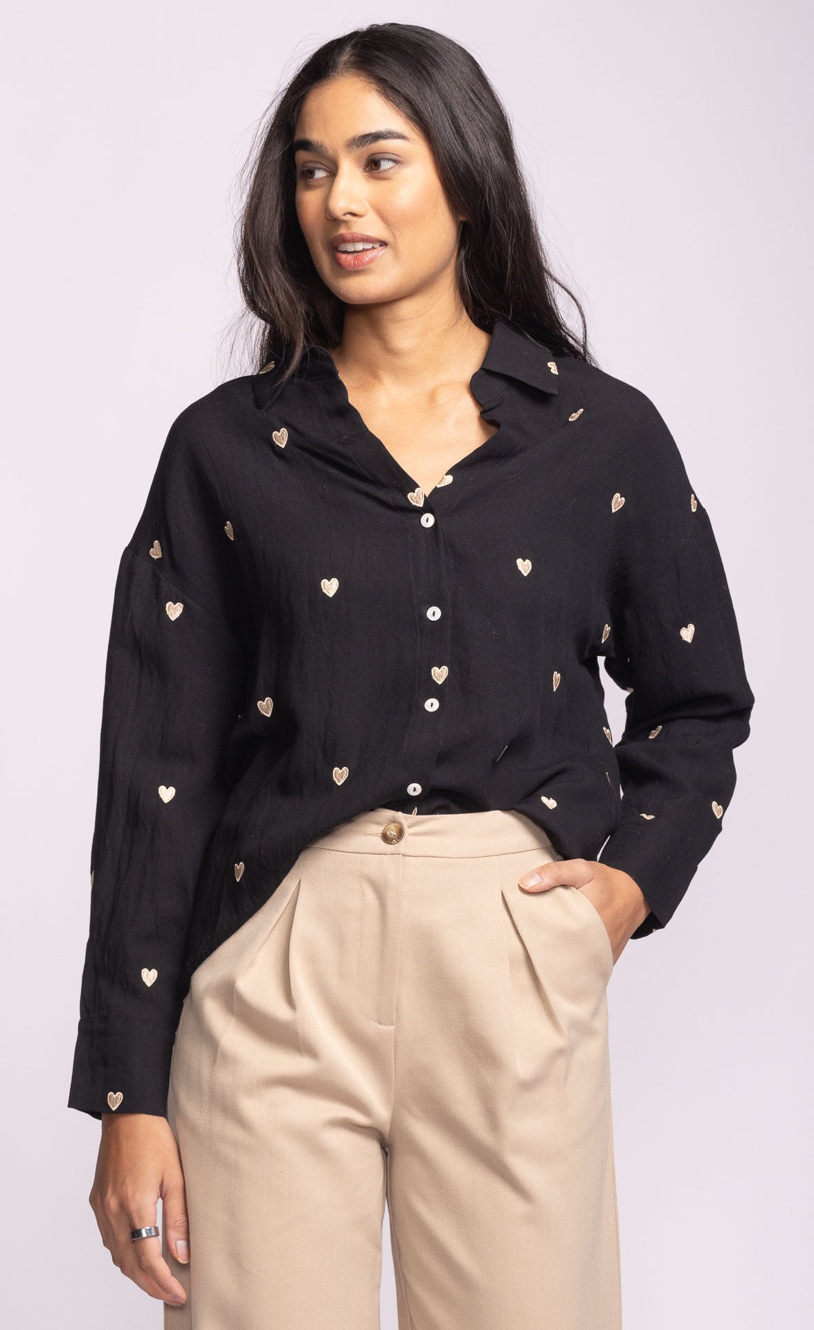 Woman wearing a black blouse with heart patterns and beige pants on a white background