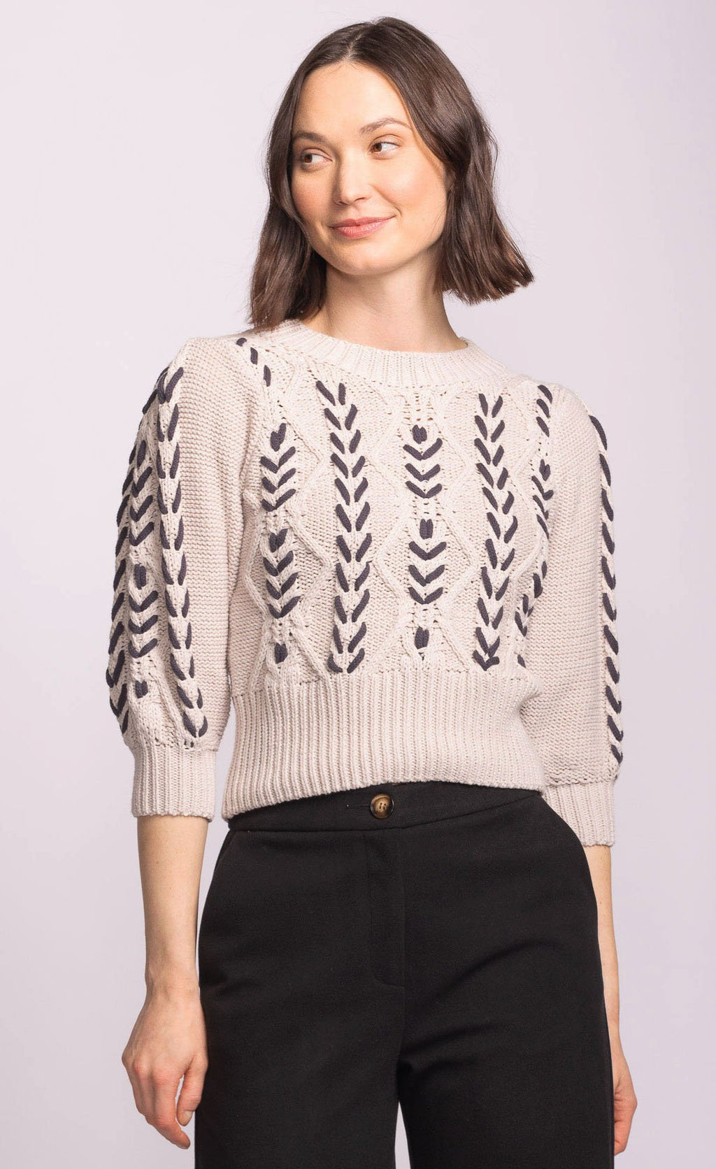 Woman wearing a cream sweater with black leaf patterns on a light gray background