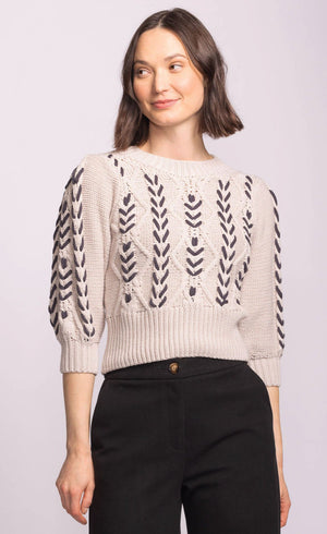 Woman wearing a cream sweater with black leaf patterns on a light gray background
