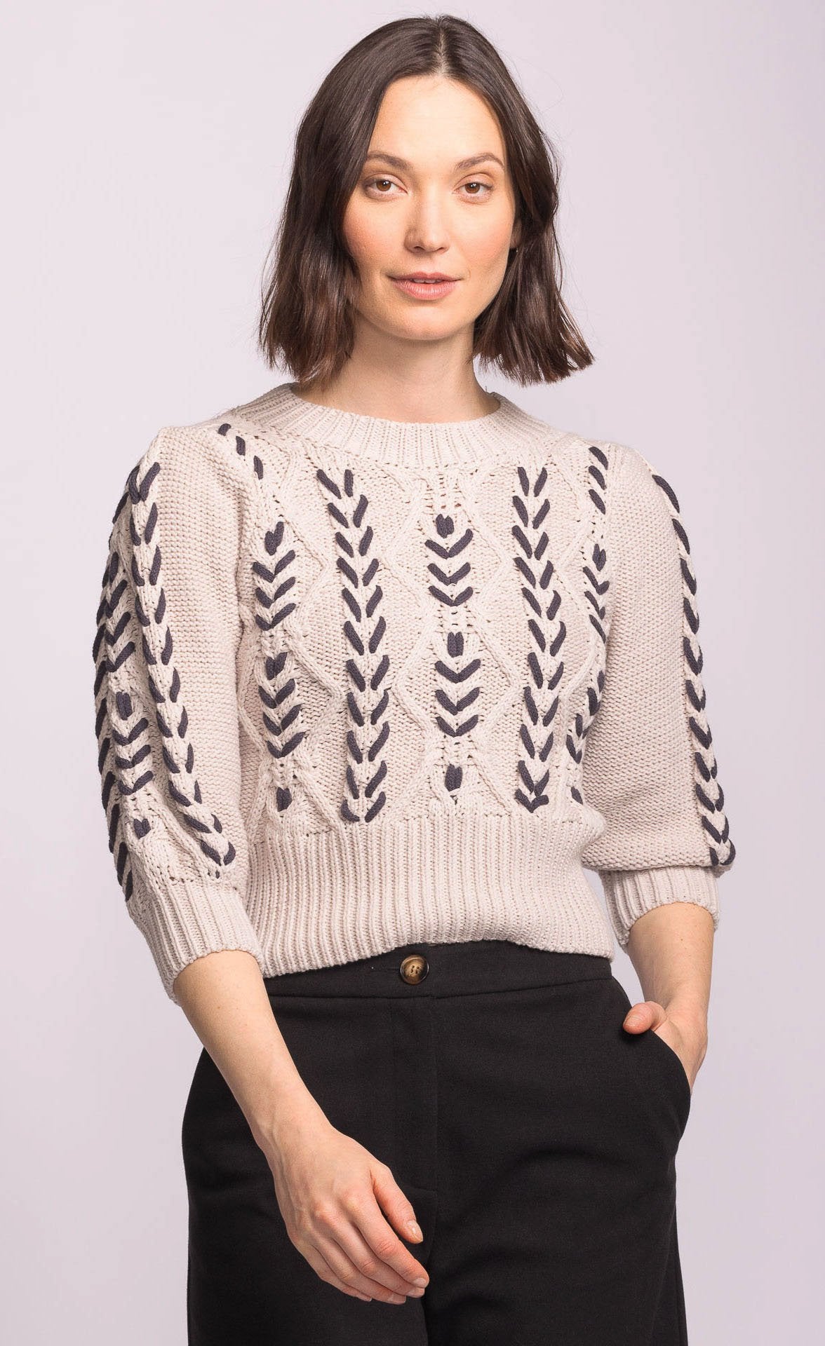 Woman wearing a beige sweater with black pattern on a light gray background