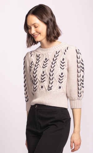 Woman wearing a beige sweater with black leaf patterns on a light pink background