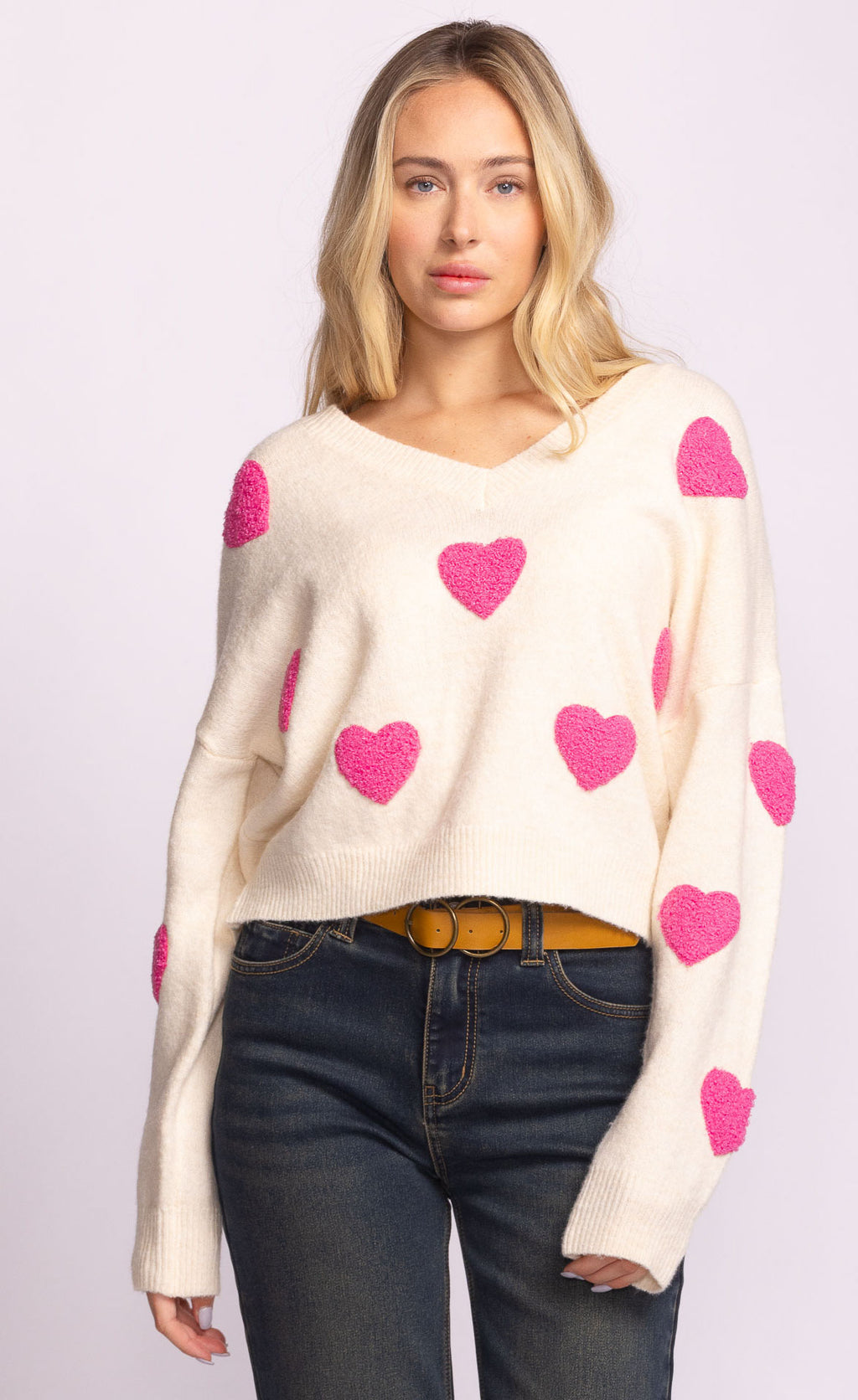 Woman wearing a cream sweater with pink heart patterns on a light purple background
