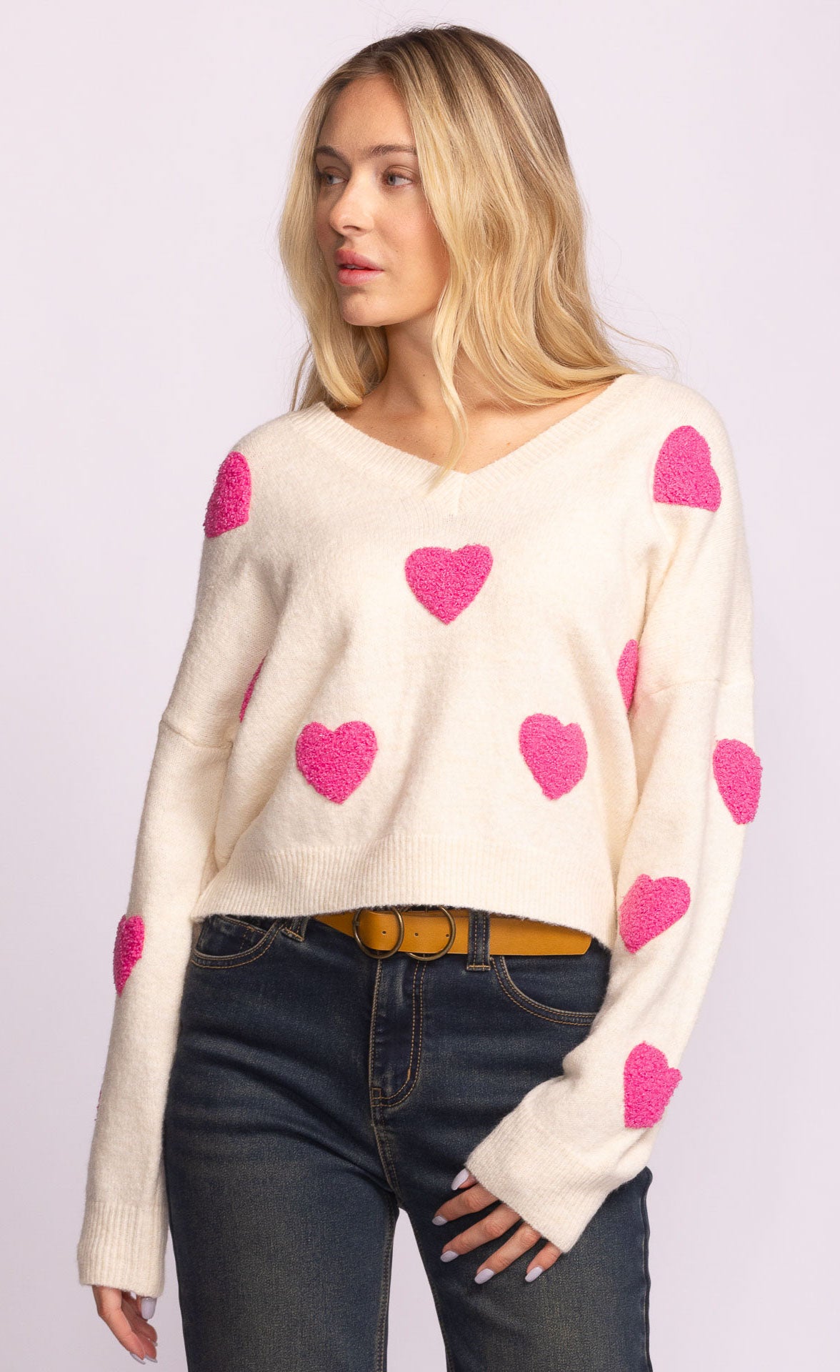 Woman wearing a cream sweater with pink heart patterns on a light purple background