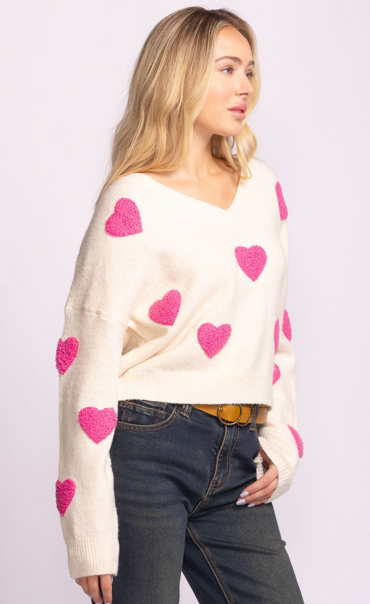 Woman wearing a cream sweater with pink heart patterns on a white background