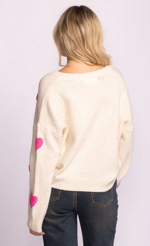 Person wearing a cream sweater with pink heart designs on a plain background