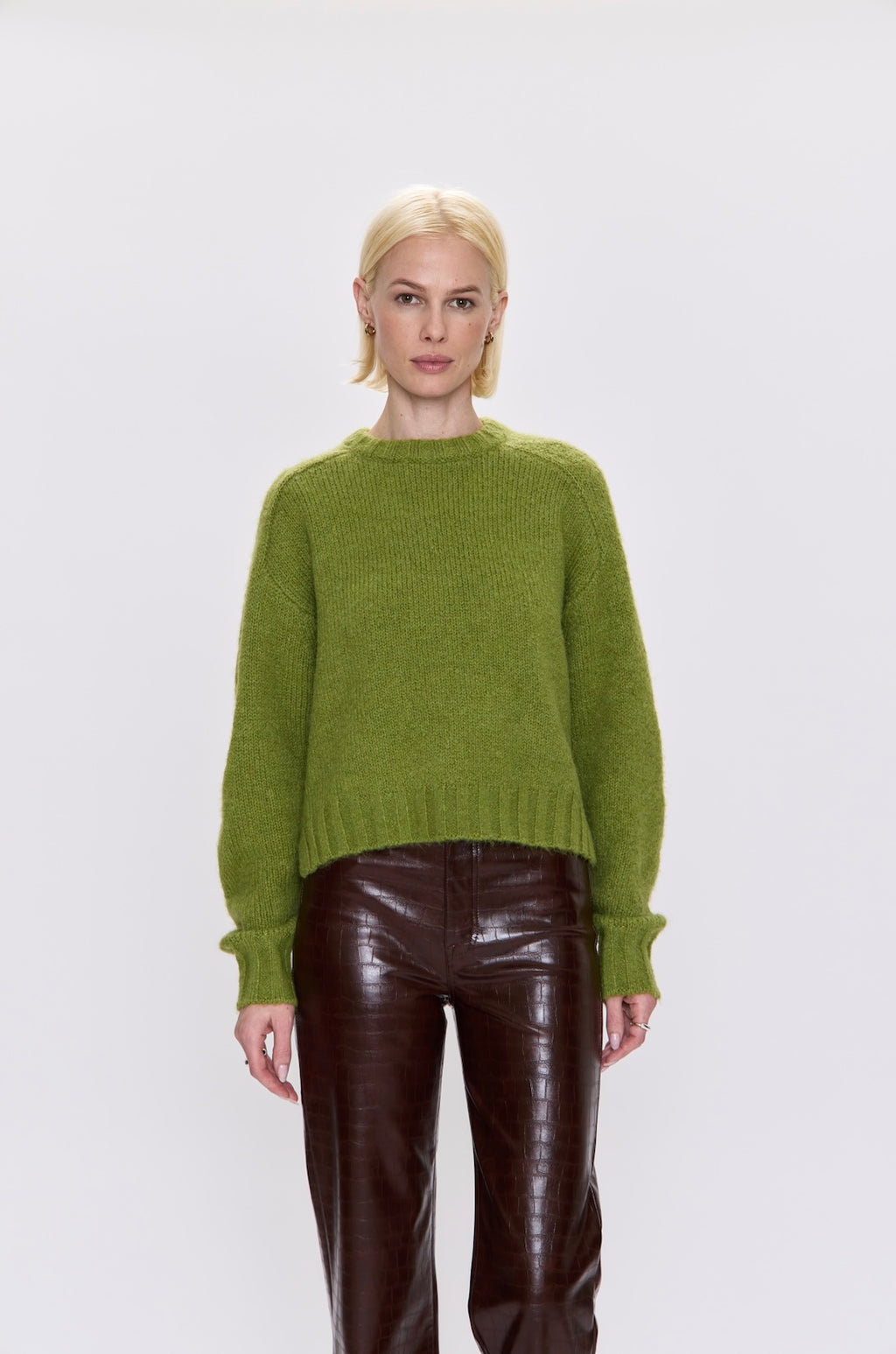 Person wearing a green sweater and brown pants on a white background