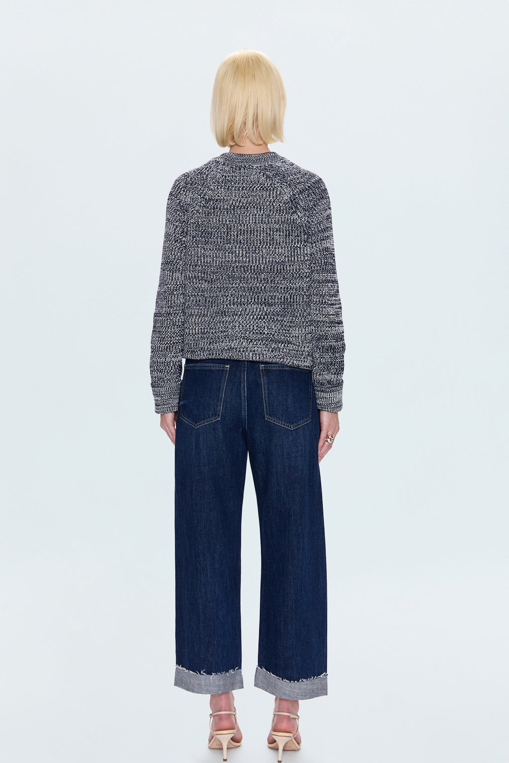 Person wearing a patterned sweater and dark jeans on a light blue background