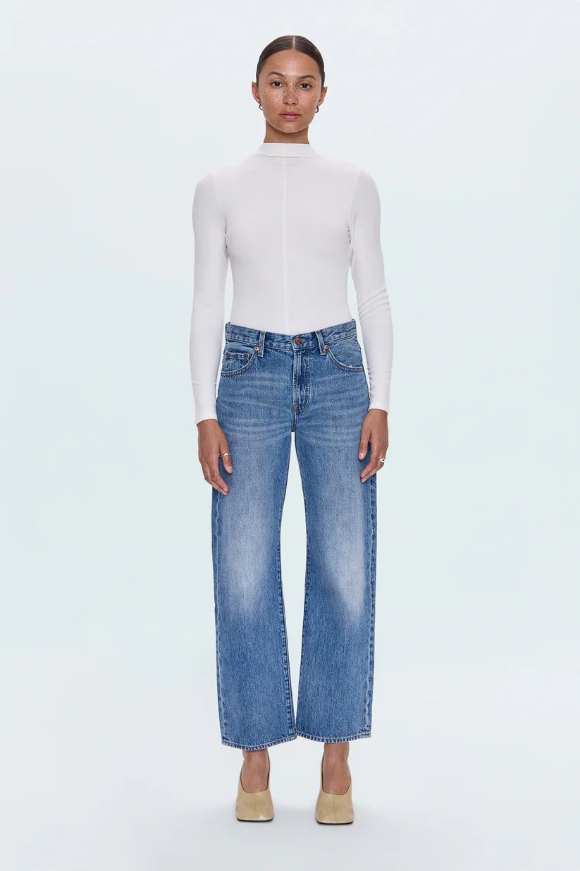 Person wearing a white turtleneck and blue jeans on a white background