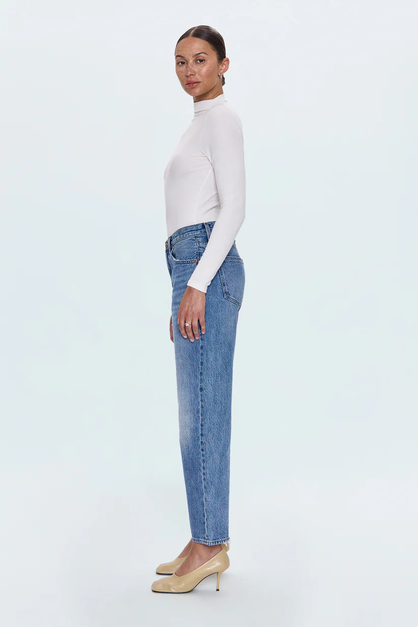 Woman wearing a white turtleneck and blue jeans on a light gray background