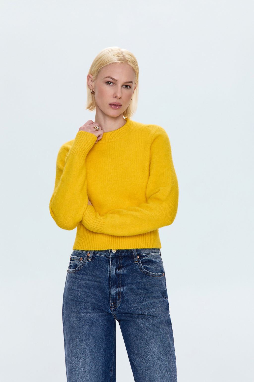 Woman wearing a yellow sweater and blue jeans against a light gray background