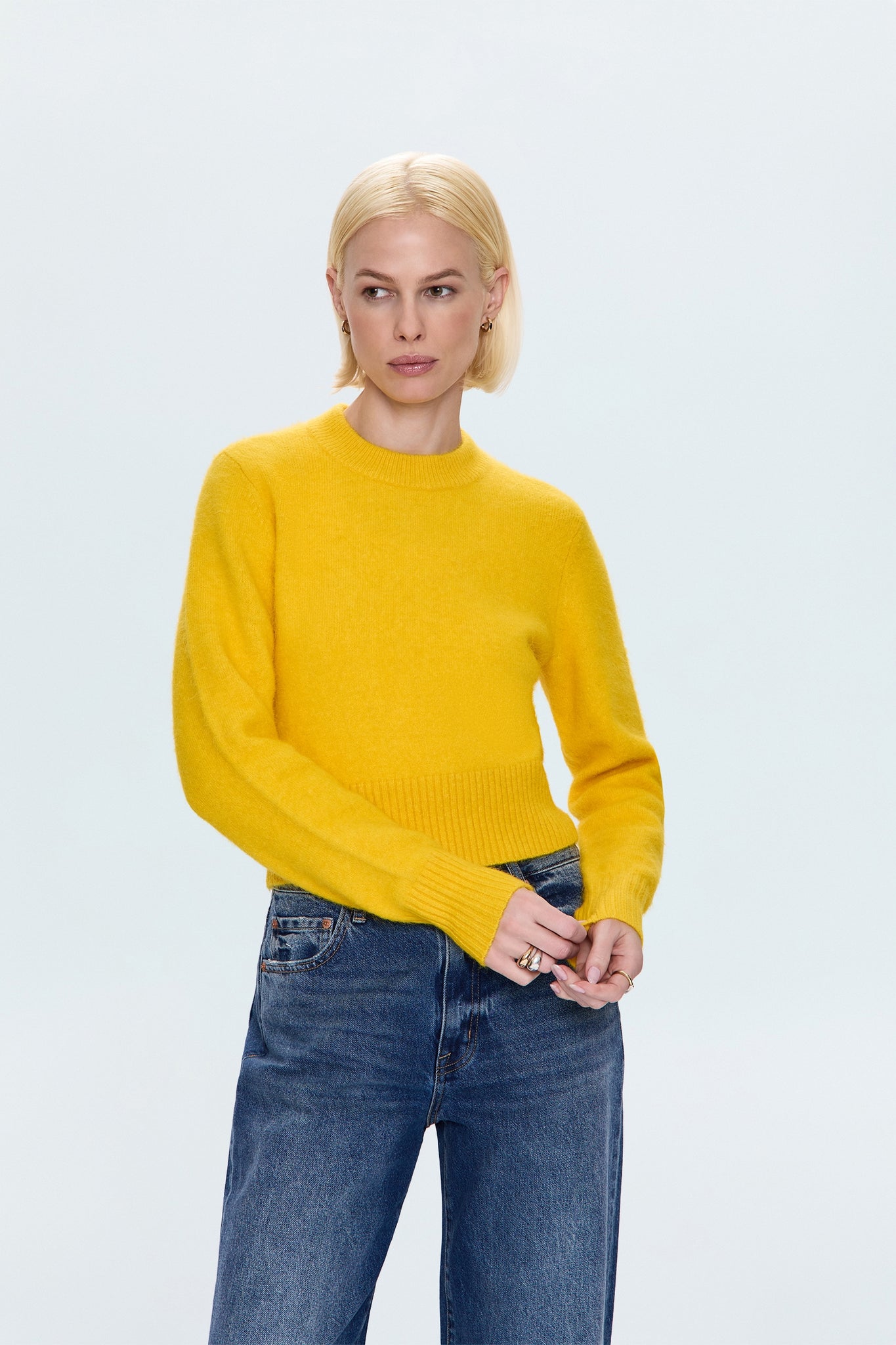 Person wearing a yellow sweater and blue jeans on a light gray background