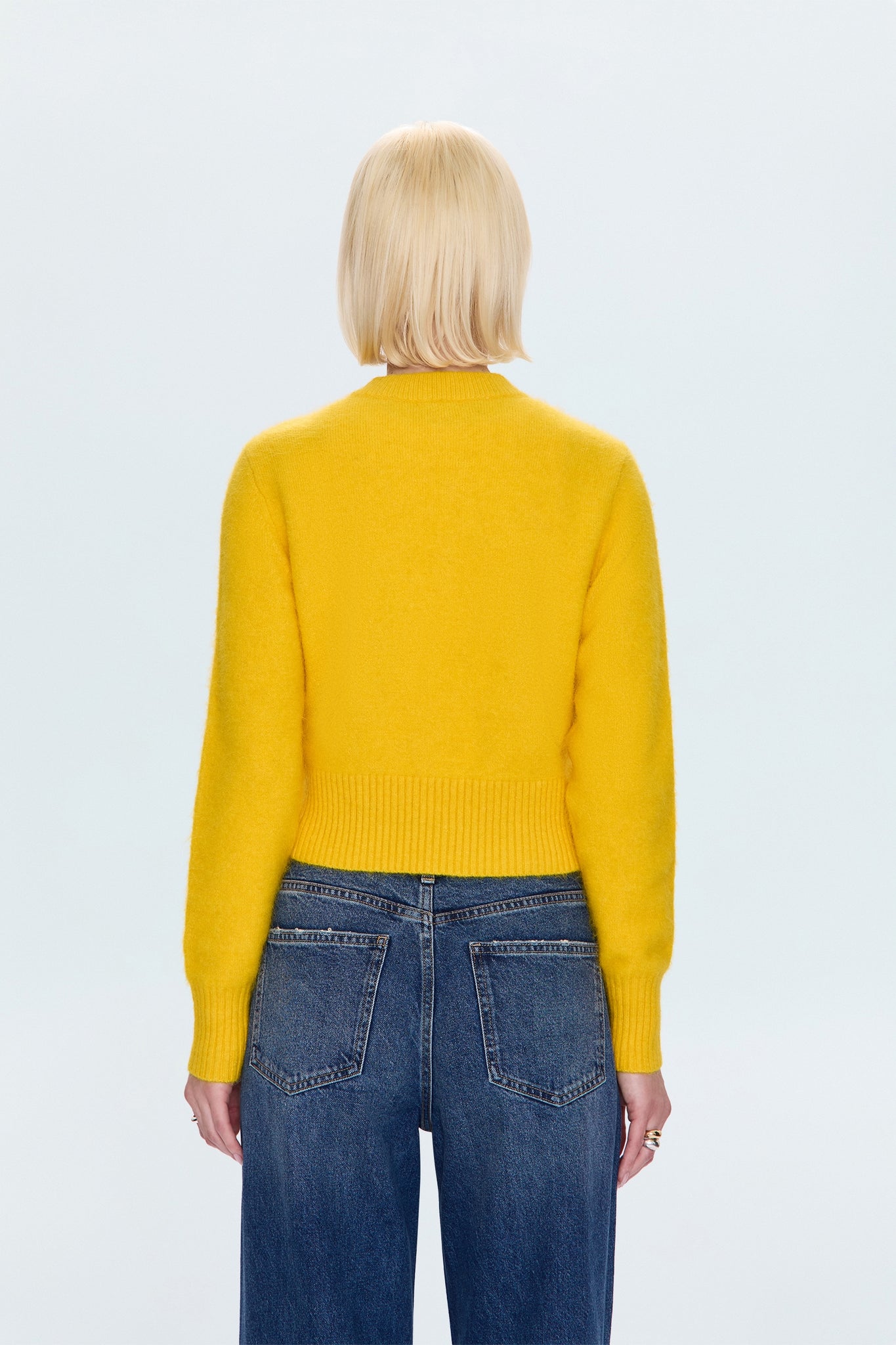Person wearing a yellow sweater and blue jeans on a light gray background