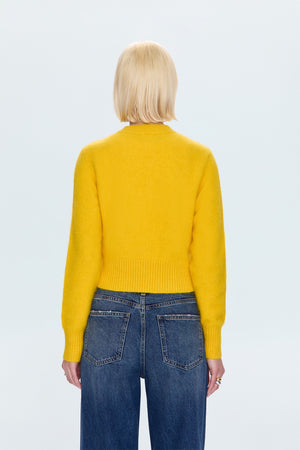 Person wearing a yellow sweater and blue jeans on a light gray background