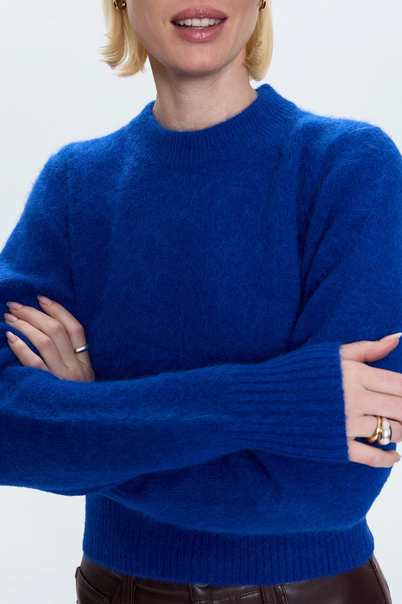 Person wearing a blue sweater with arms crossed on a white background