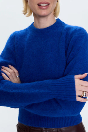 Person wearing a blue sweater with arms crossed on a white background