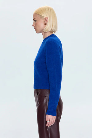 Person wearing a blue sweater and brown pants on a light gray background