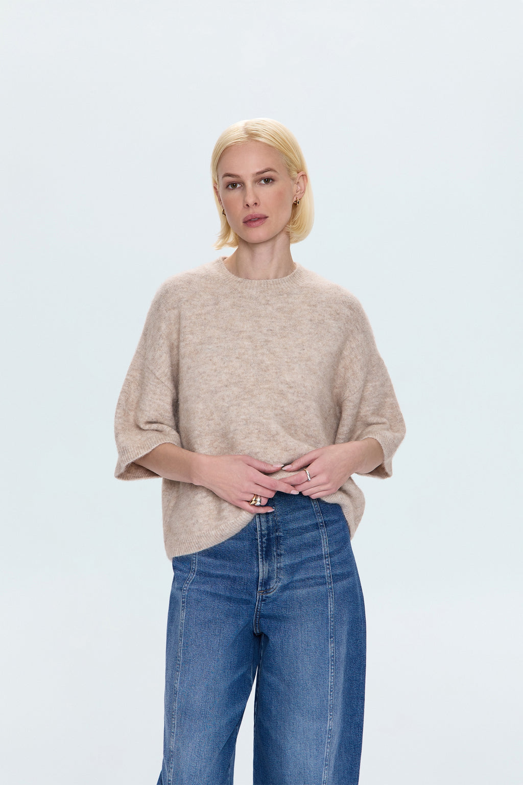 Woman wearing a beige sweater and blue jeans on a light gray background