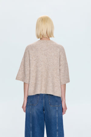 Person wearing a beige sweater and blue jeans on a light gray background