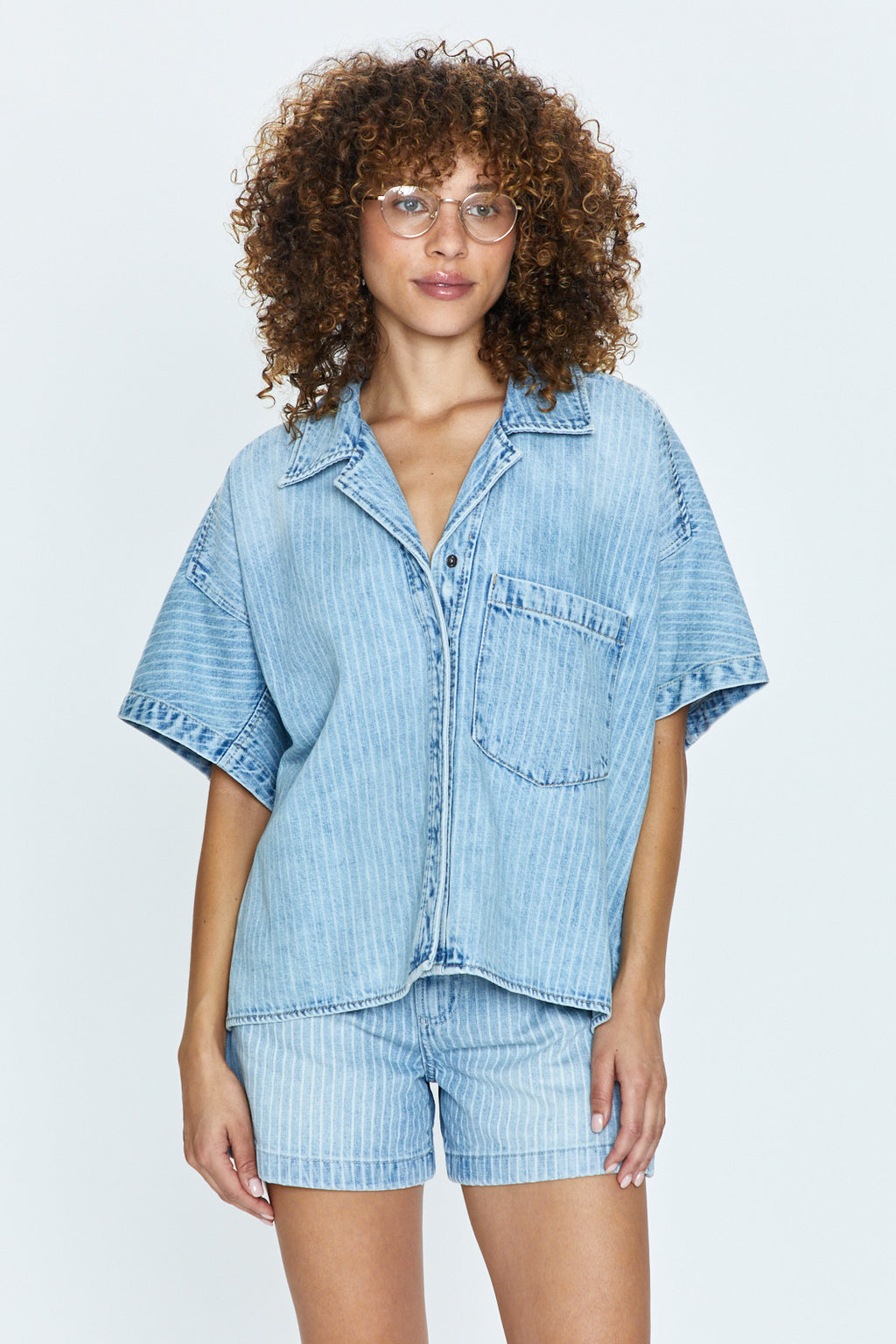 Relaxed fit, short sleeve denim shirt with a camp collar neckline and exaggerated, dropped shoulders. Constructed with a high-low split crop length, and crafted from a clean, medium blue denim wash.