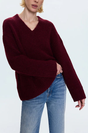 Person wearing a burgundy sweater and blue jeans on a white background