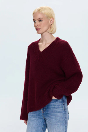Woman wearing a burgundy sweater and blue jeans on a light gray background