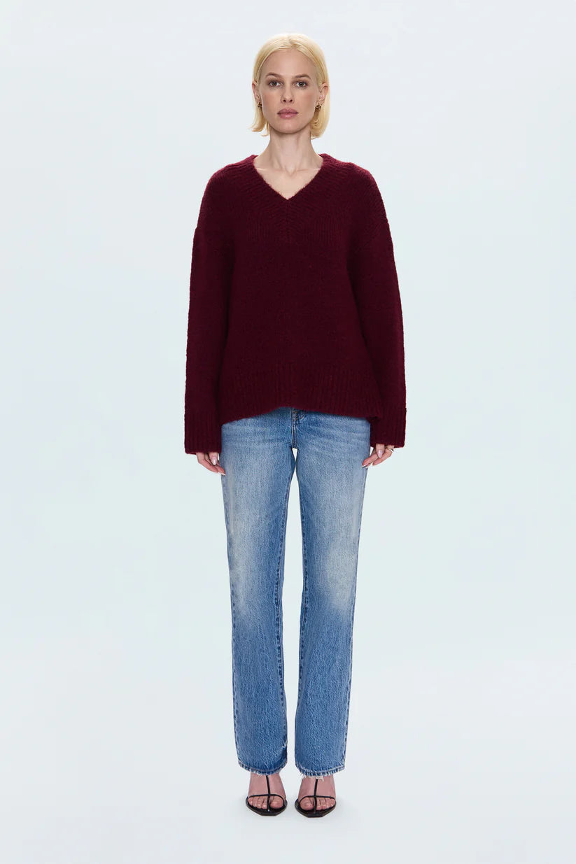 Person wearing a burgundy sweater and blue jeans on a white background