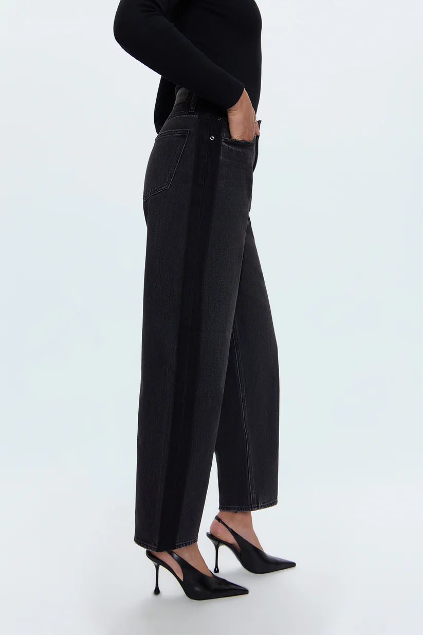 Person wearing black high-waisted jeans and black shoes on a light blue background