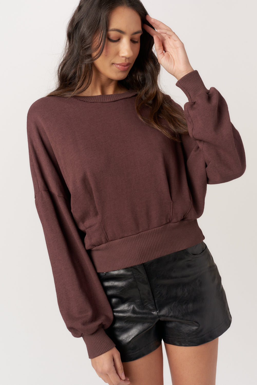 Woman wearing a brown oversized sweater and black leather shorts on a white background