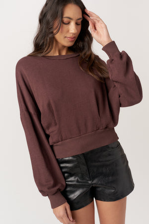 Woman wearing a brown oversized sweater and black leather shorts on a white background