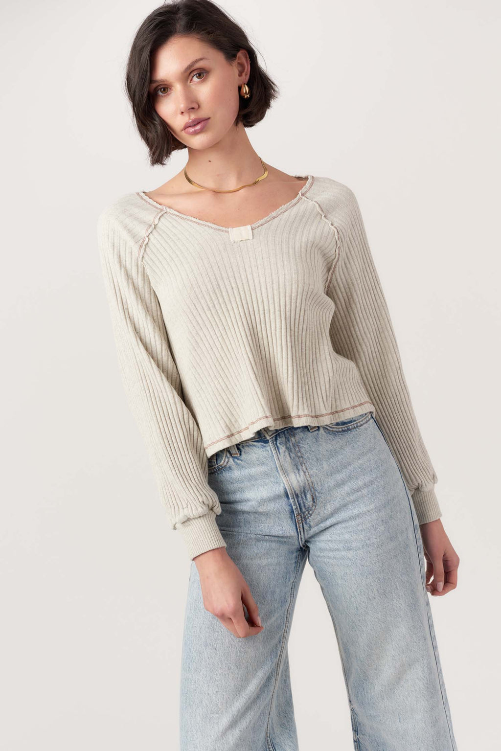 Woman wearing a beige ribbed sweater and light blue jeans on a white background