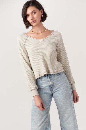Woman wearing a beige ribbed sweater and light blue jeans on a white background