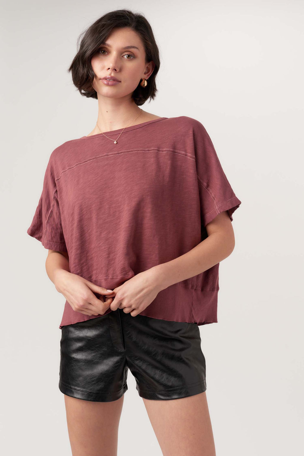 Woman wearing a loose-fitting maroon top and black leather shorts on a plain background