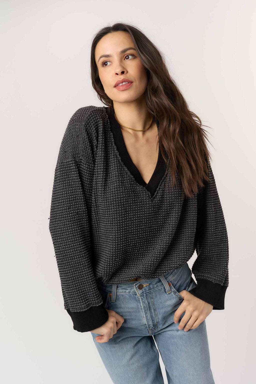 Woman wearing a black patterned sweater and blue jeans against a white background