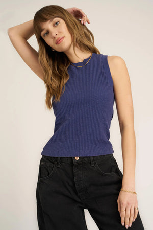 Woman wearing a blue sleeveless top and black pants against a plain background