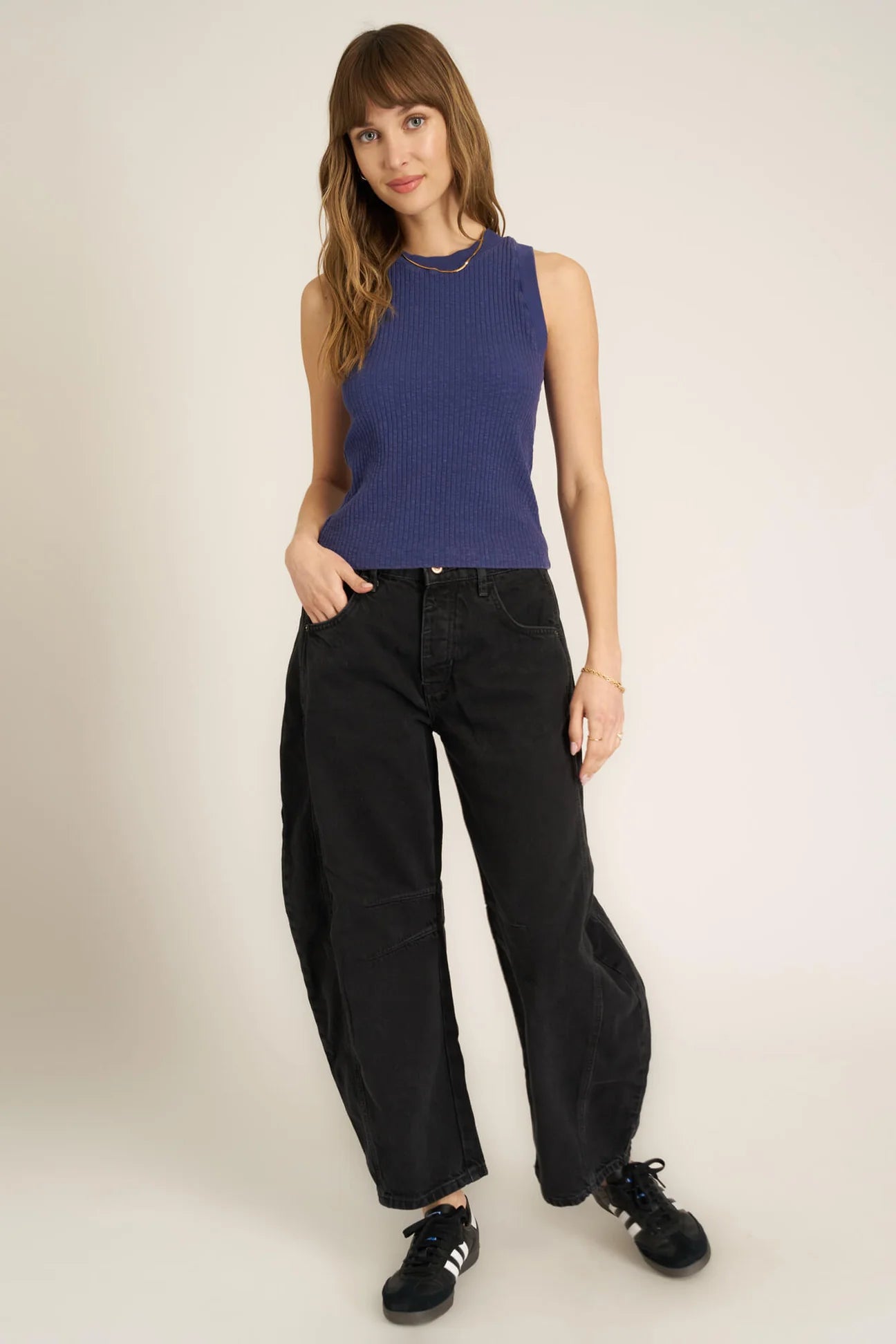 Woman wearing a blue sleeveless top and black pants on a white background