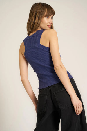 Woman wearing a blue sleeveless top and black pants against a plain background