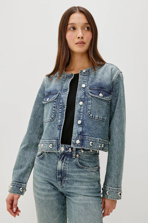 Woman wearing a denim jacket and jeans on a plain background