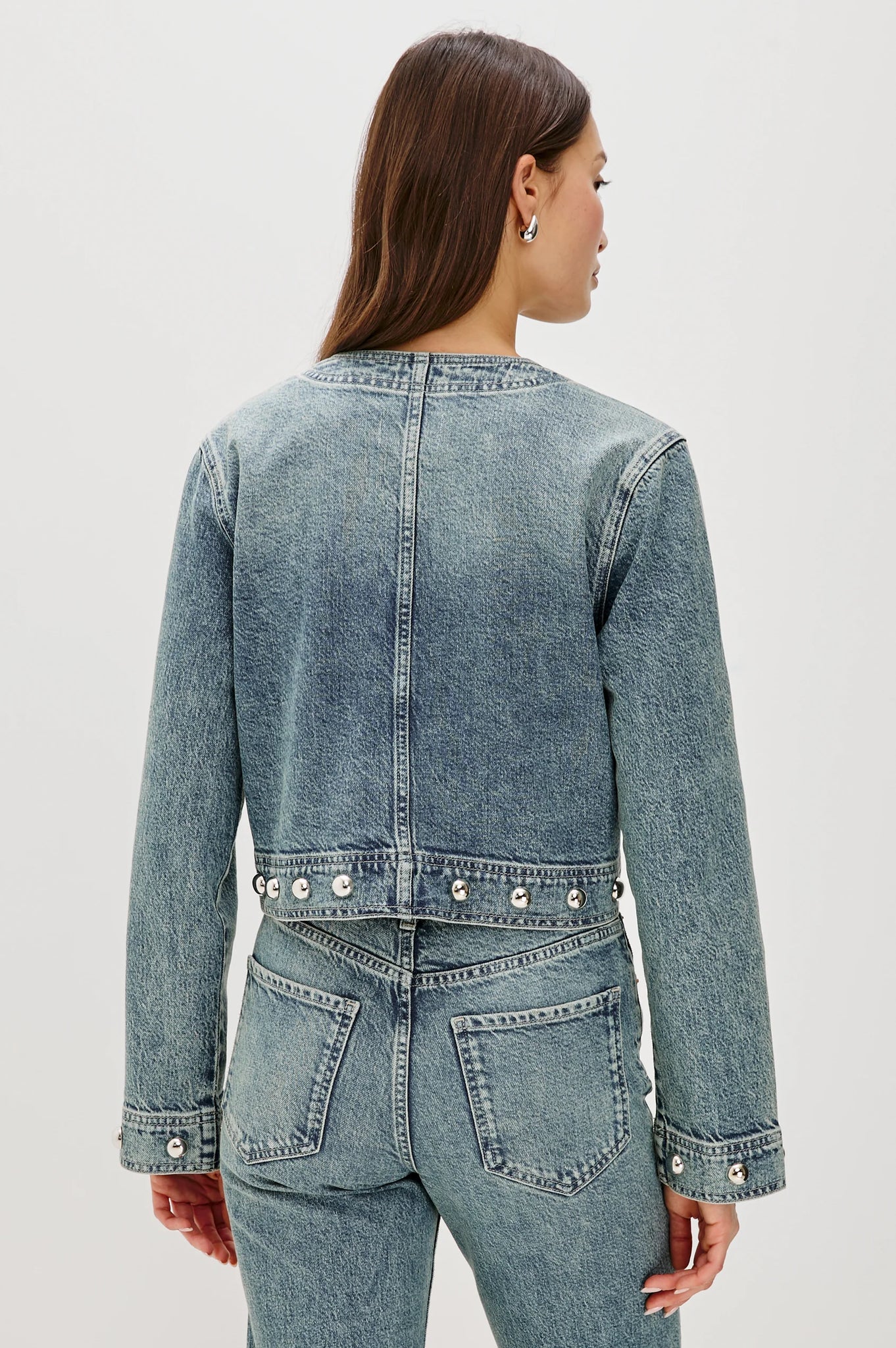 Person wearing a blue denim jacket and jeans on a white background