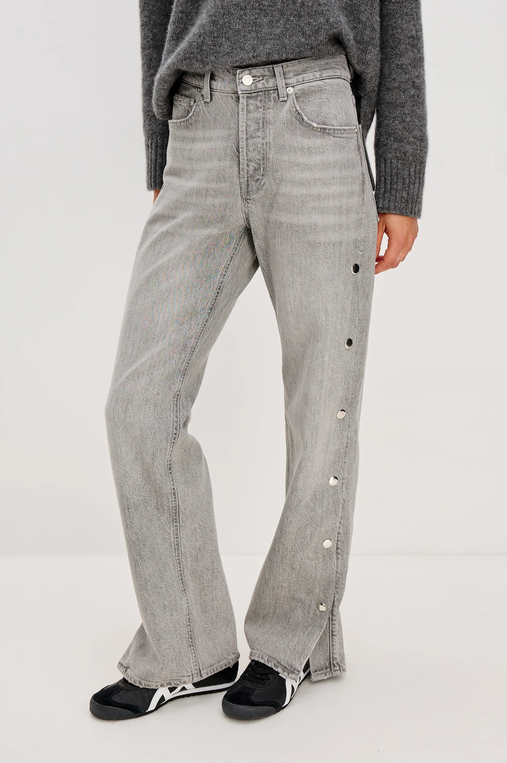 Person wearing gray jeans with button details on a white background