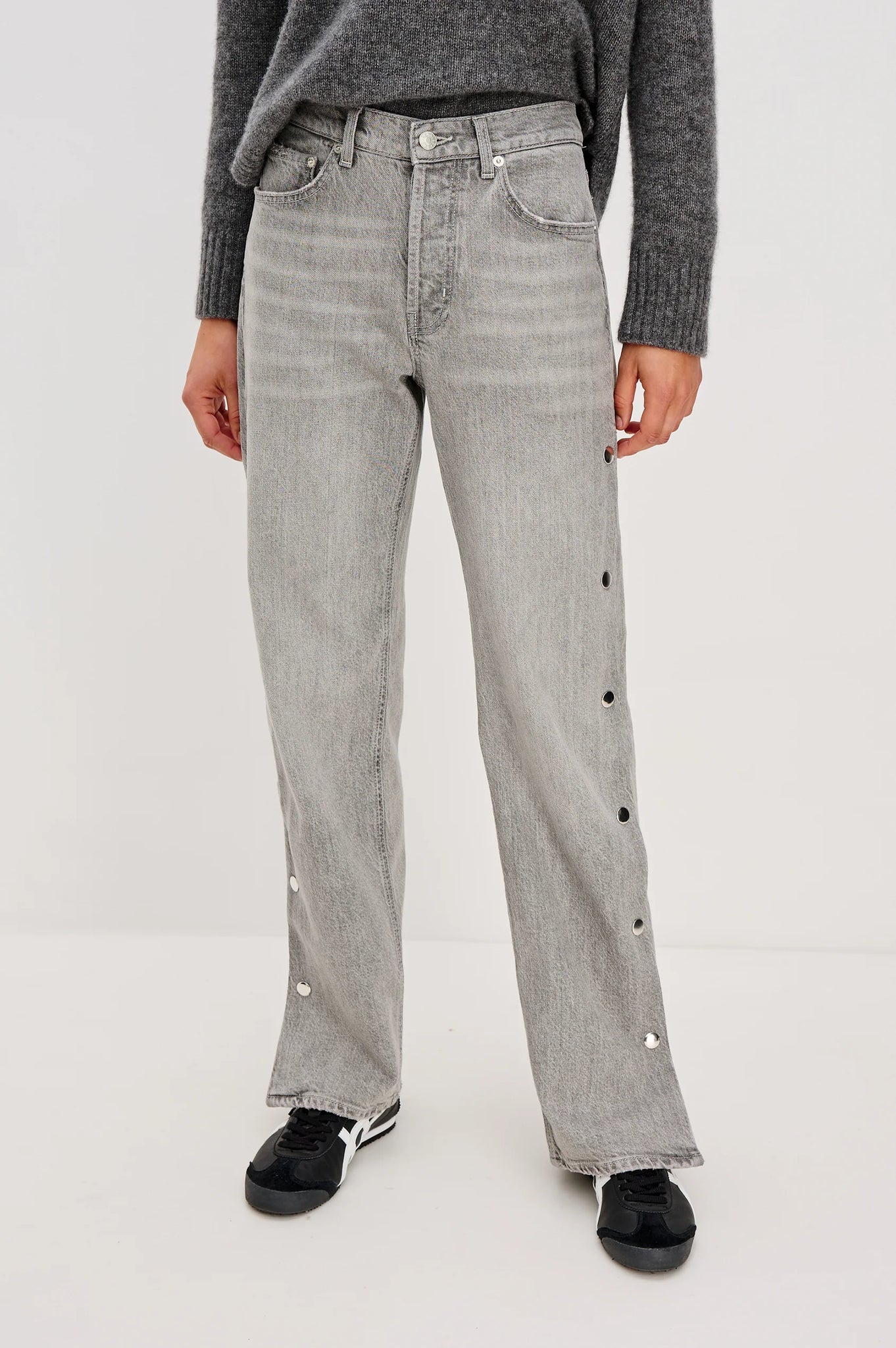Person wearing gray jeans with decorative buttons on a white background