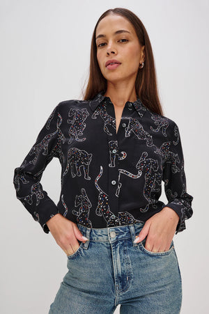 Woman wearing a black patterned shirt and blue jeans on a white background