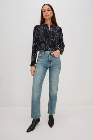 Woman wearing a black patterned blouse and blue jeans on a white background