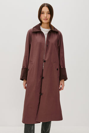 Woman wearing a long brown coat on a white background