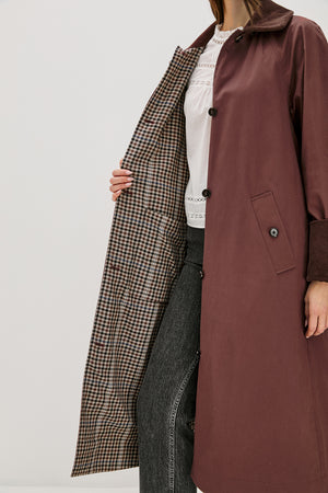 Person wearing a long brown coat with a plaid pattern on a white background