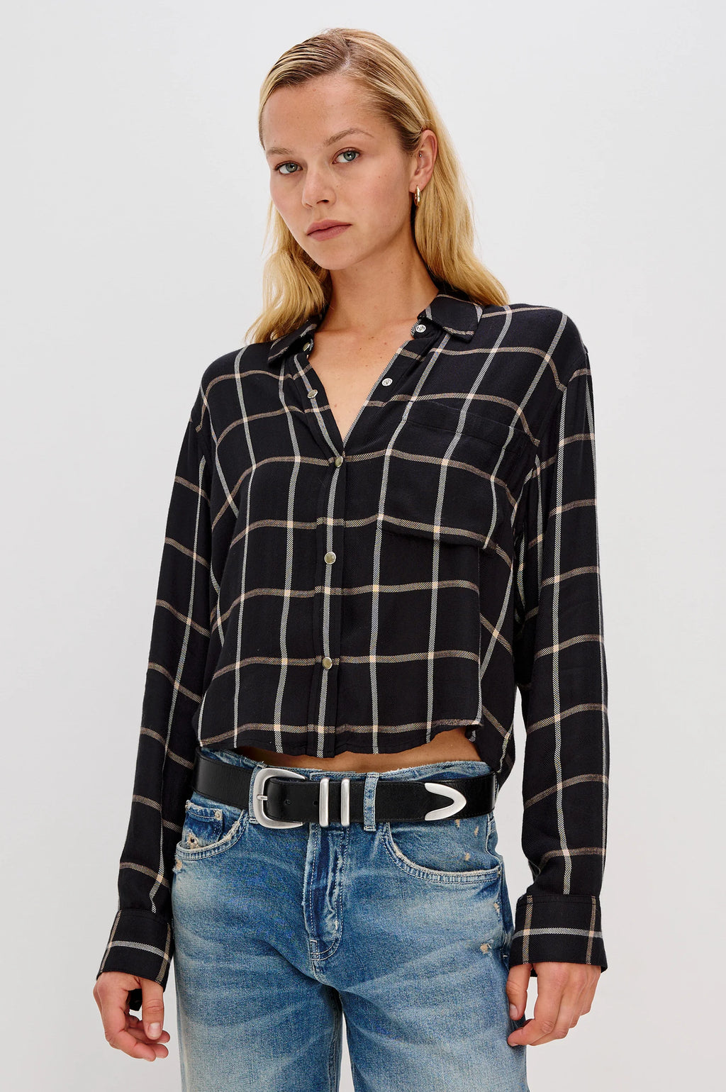 Woman wearing a black and white checkered shirt and blue jeans on a light gray background