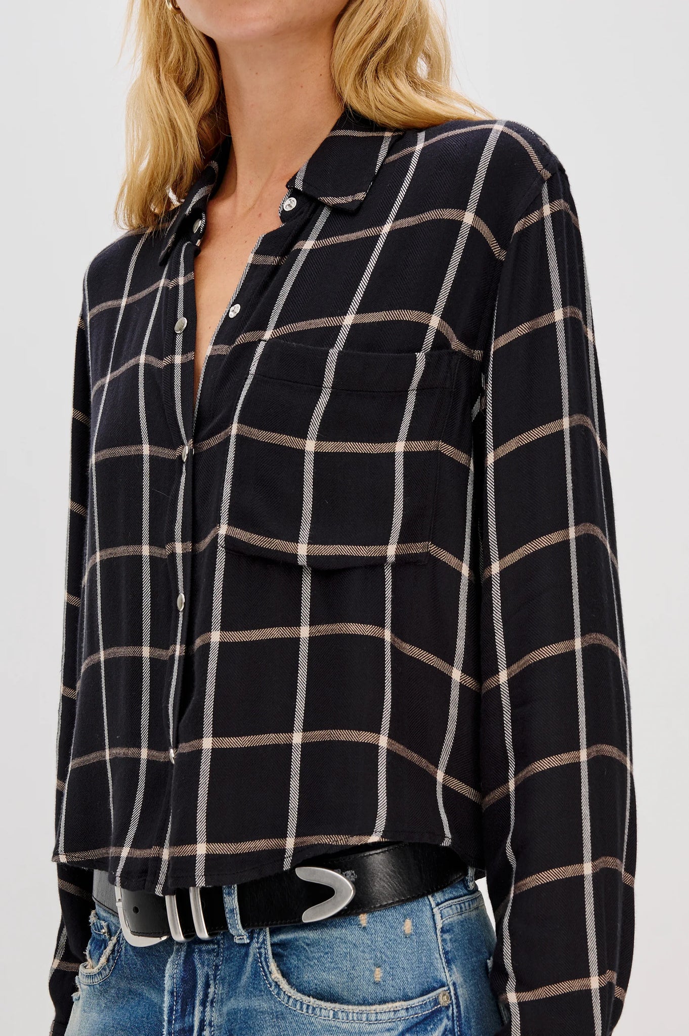 Person wearing a black and beige plaid shirt with blue jeans on a white background
