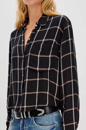Person wearing a black and beige plaid shirt with blue jeans on a white background