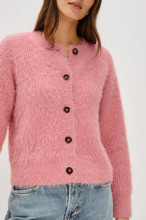 Person wearing a pink textured cardigan with black buttons on a white background