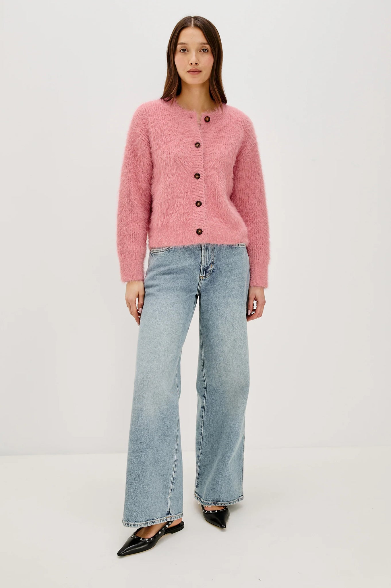 Woman wearing a pink cardigan and blue jeans on a white background